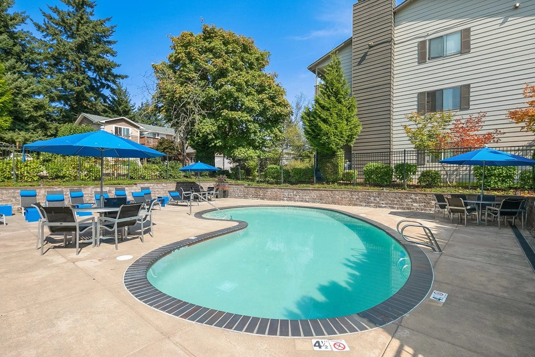 Pool with deck seating and umbrellas surrounded by large trees