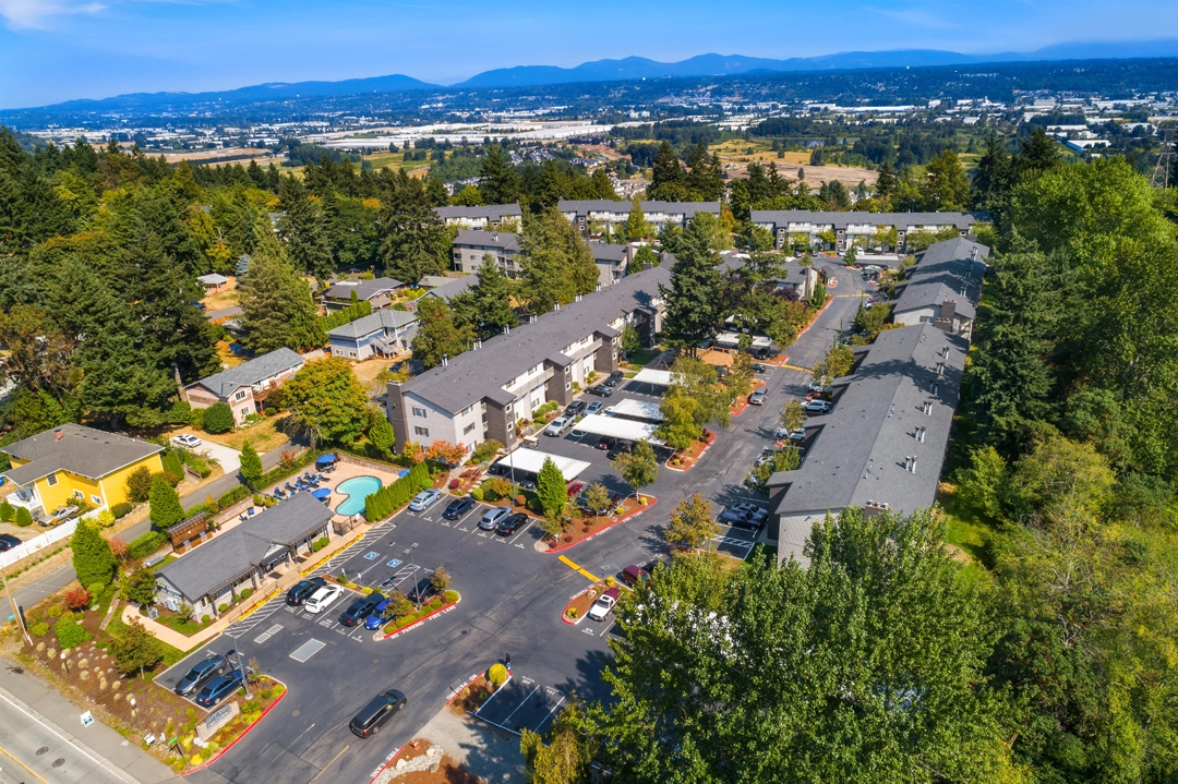 Aerial view of the property with lots of trees, community pool, and covered parking stalls